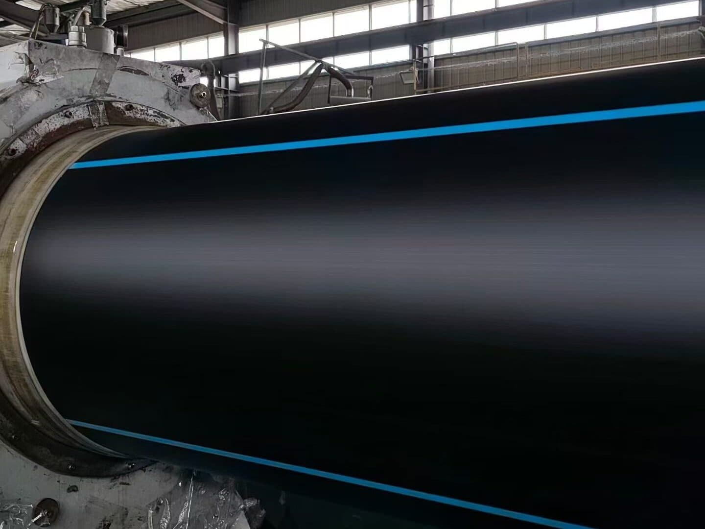 A large-diameter black PE100 pipe with blue stripes emerging from the vacuum calibration tank