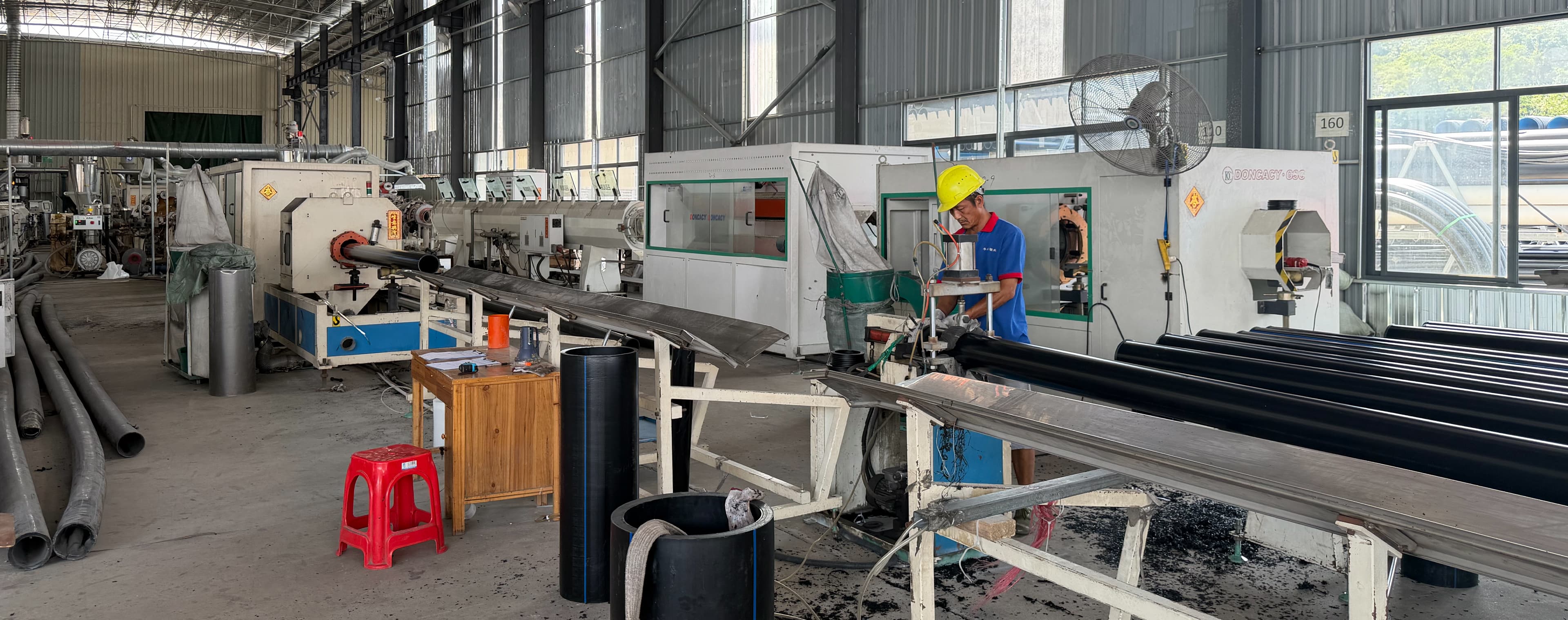 عامل يشغّل منشار القطع في خط بثق أنابيب HDPE، وإلى جانبه أنابيب PE100 سوداء على الحوامل
