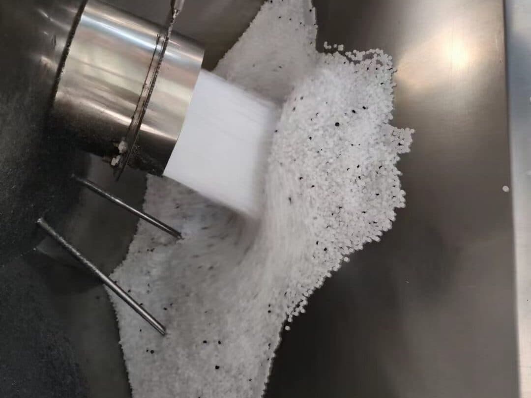 White PE100 compound granules with black masterbatch pellets pouring into a stainless-steel feed hopper